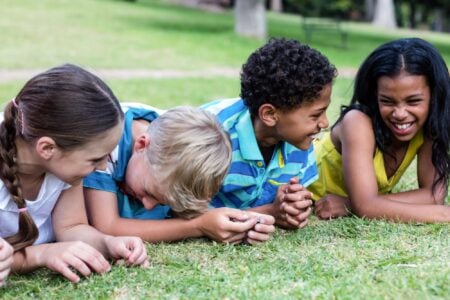 Four happy kids lying on the grass in the park.