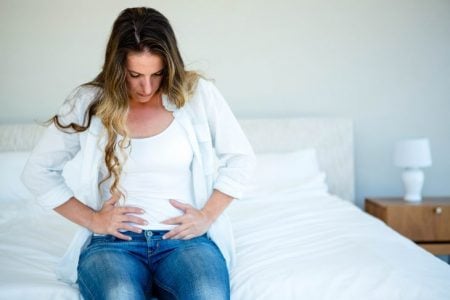 Woman sitting on her bed holding her stomach in discomfort