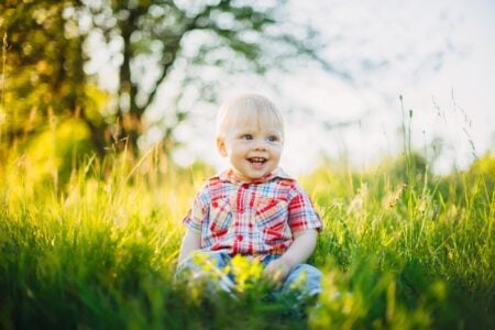 A boy wearing red tartan shirt sitting on the grass in the park.