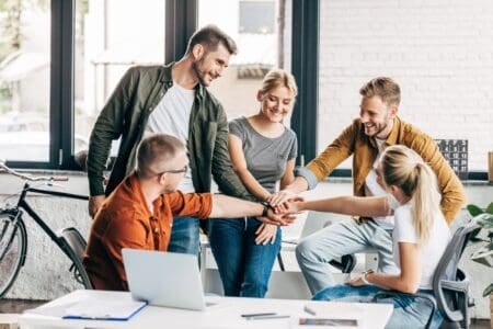 Group of five people making team gesture in work setting