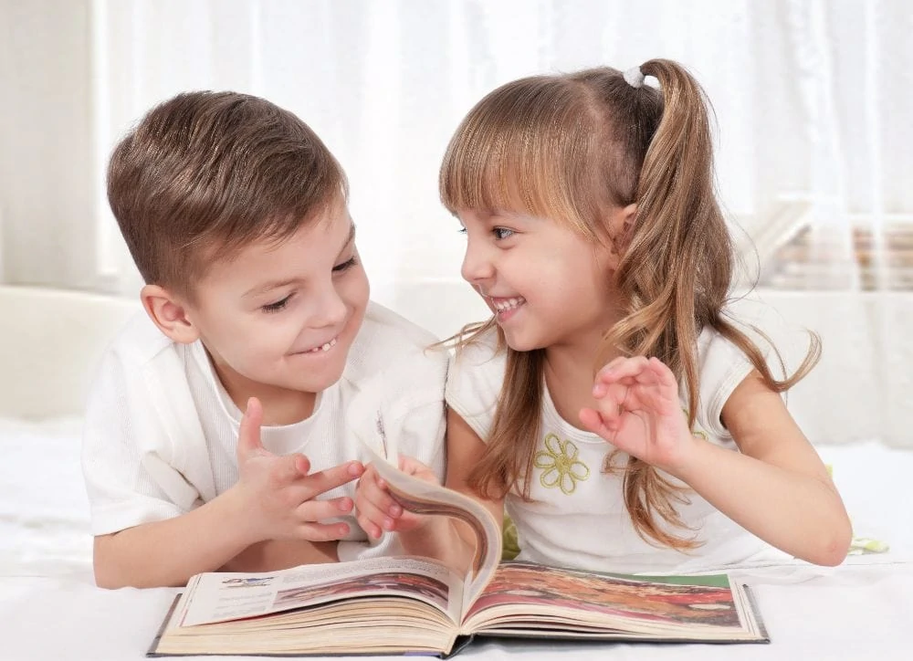 Two cute preschoolers in white reading a picture book