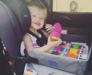 Smiling toddler playing with a travel tray in her car seat