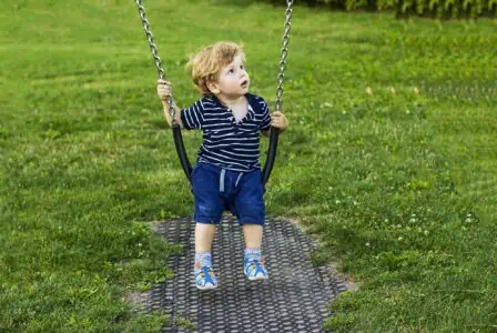 Cute blonde boy on swing in the park