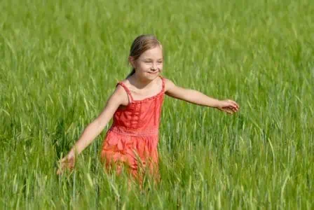 Adorable young girl in red dress running on green field