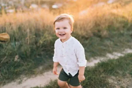Cute little toddler boy smiling at the camera on sunset in green field