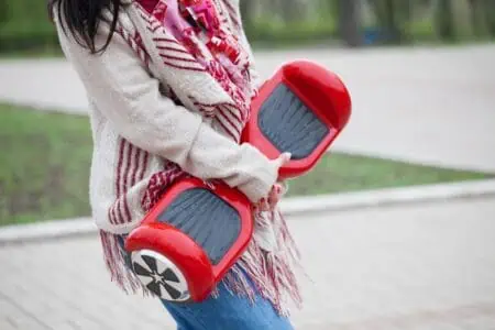 Woman holding modern red hoverboard in hands while walking in the park