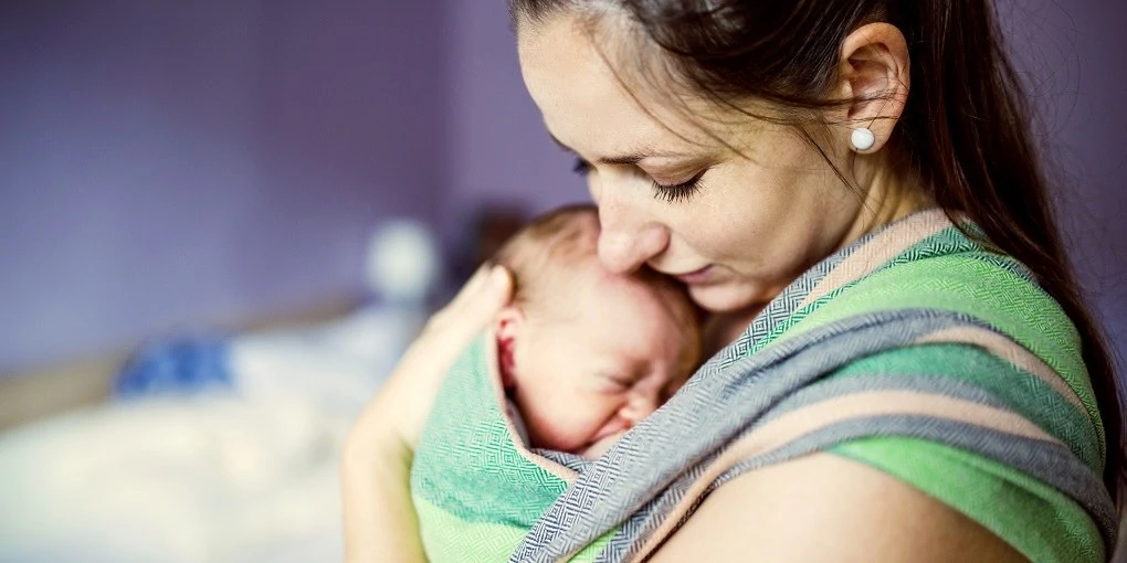 Newborn baby held by mother in baby carrier