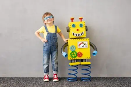 Happy child in denim jumper standing beside robot toy