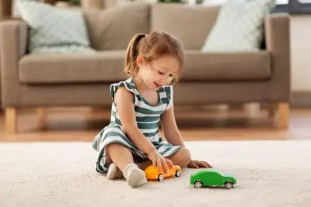Toddler girl playing with toy car sitting on the floor at home